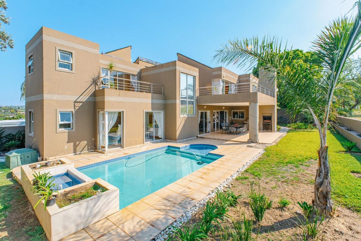 Spacious rear exterior featuring a swimming pool, covered patio with built-in braai, and upper-level balconies overlooking the landscaped garden.