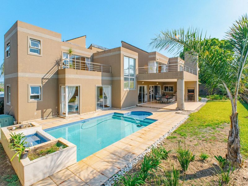 Spacious rear exterior featuring a swimming pool, covered patio with built-in braai, and upper-level balconies overlooking the landscaped garden.