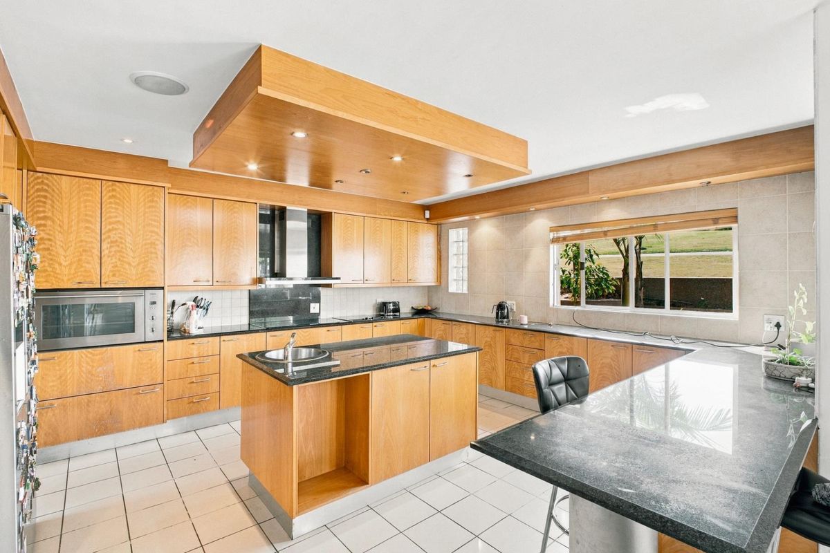 Spacious kitchen featuring warm wooden cabinetry, granite countertops, a central island, built-in appliances, and tiled flooring with ample natural light.