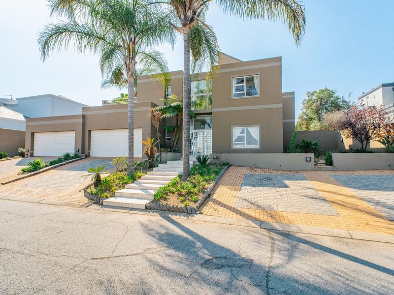 Modern double-story residence featuring a paved driveway, double garage, landscaped front garden with palm trees, and a central tiled entrance staircase.