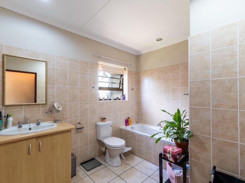 A functional bathroom featuring a built-in bathtub, vanity cabinet with basin, toilet, and neutral wall and floor tiling.