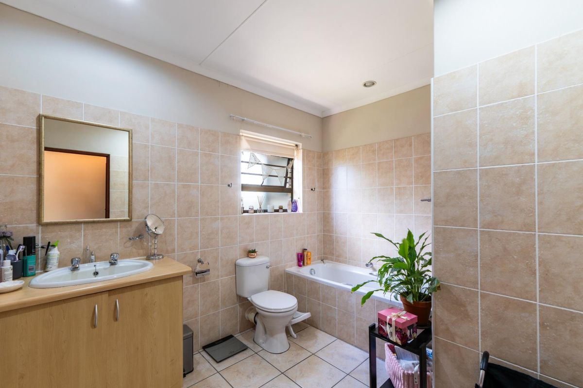 A functional bathroom featuring a built-in bathtub, vanity cabinet with basin, toilet, and neutral wall and floor tiling.