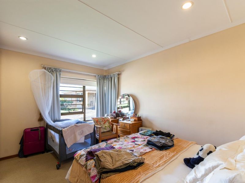 A functional bedroom featuring built-in cupboards, recessed downlighting, and a large window providing natural light.
