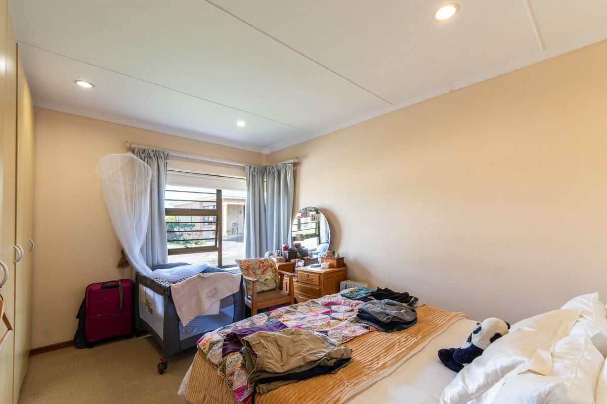 A functional bedroom featuring built-in cupboards, recessed downlighting, and a large window providing natural light.