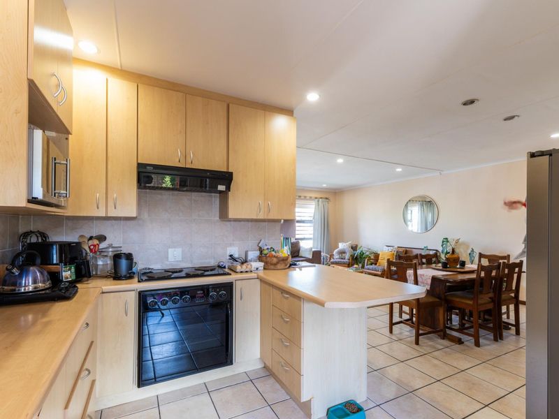 Open-plan kitchen and dining area featuring light wood cabinetry, built-in oven and hob, tiled flooring, and recessed lighting throughout the space.