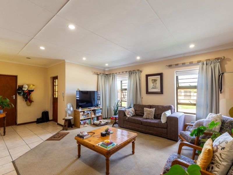 A spacious living room featuring a combination of tiled and carpeted flooring, recessed downlights, and large windows allowing for natural light.