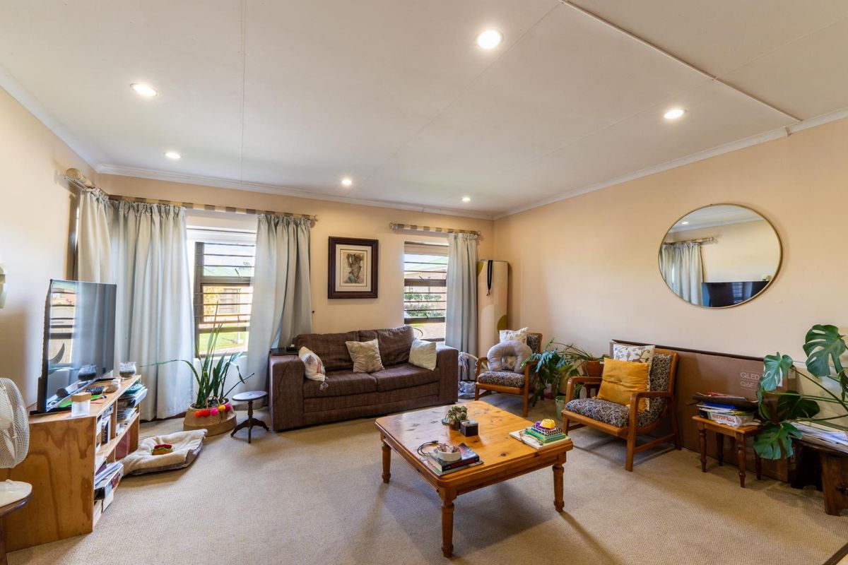 A spacious living room featuring neutral carpeting, recessed downlighting, and large windows that provide natural light to the area.