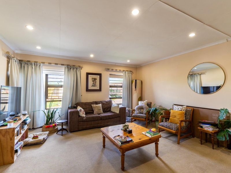 A spacious living room featuring neutral carpeting, recessed downlighting, and large windows that provide natural light to the area.