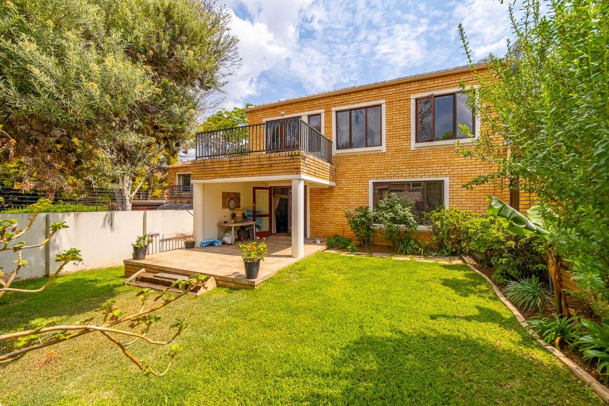Rear view of a two-story brick house featuring a ground-level tiled patio, an upper-level balcony, and a well-maintained garden area.