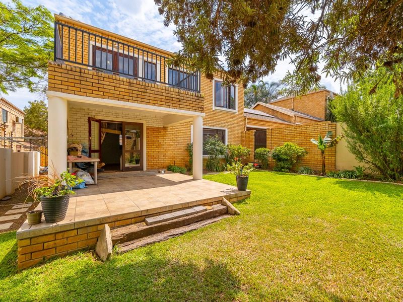 Rear view of a double-story brick house featuring a covered tiled patio, a balcony with metal railings, and a well-maintained garden area.