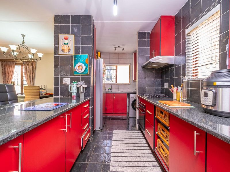 A functional kitchen featuring vibrant red cabinetry, granite countertops, a gas hob, and dark tiled flooring, offering a bold and practical workspace.