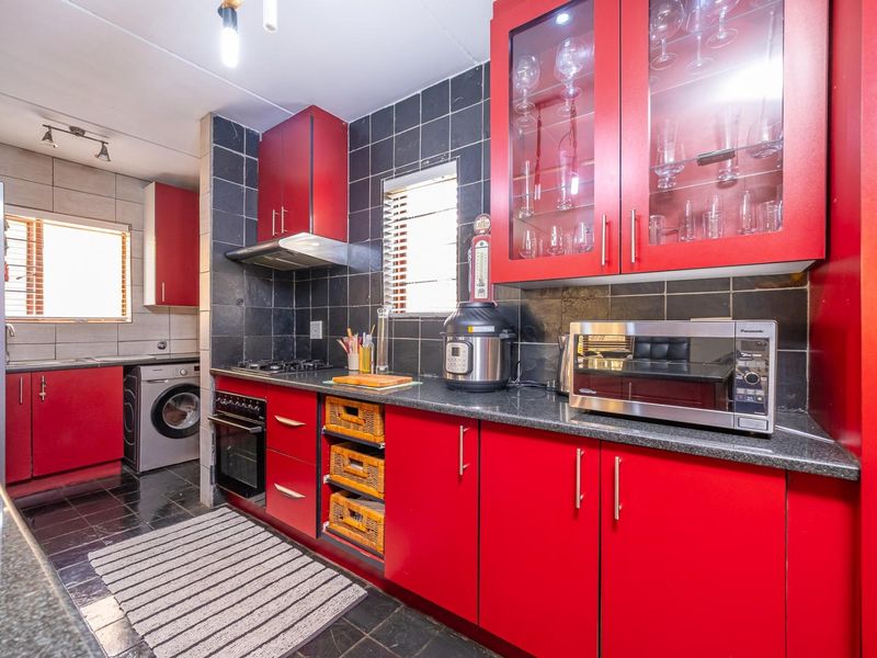 A functional kitchen featuring bold red cabinetry, granite countertops, a gas hob, and integrated laundry facilities with dark tiled flooring and splashbacks.