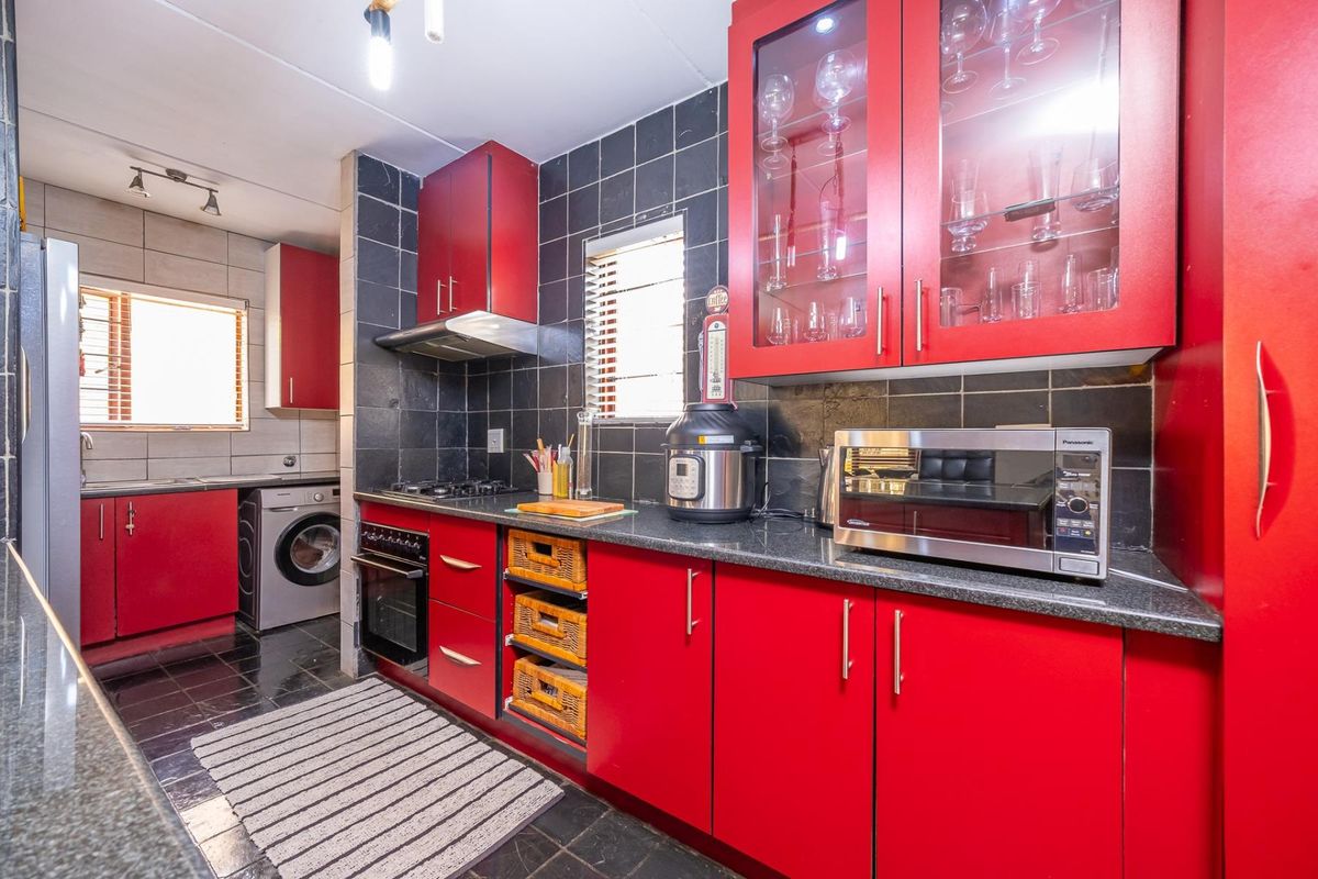 A functional kitchen featuring bold red cabinetry, granite countertops, a gas hob, and integrated laundry facilities with dark tiled flooring and splashbacks.