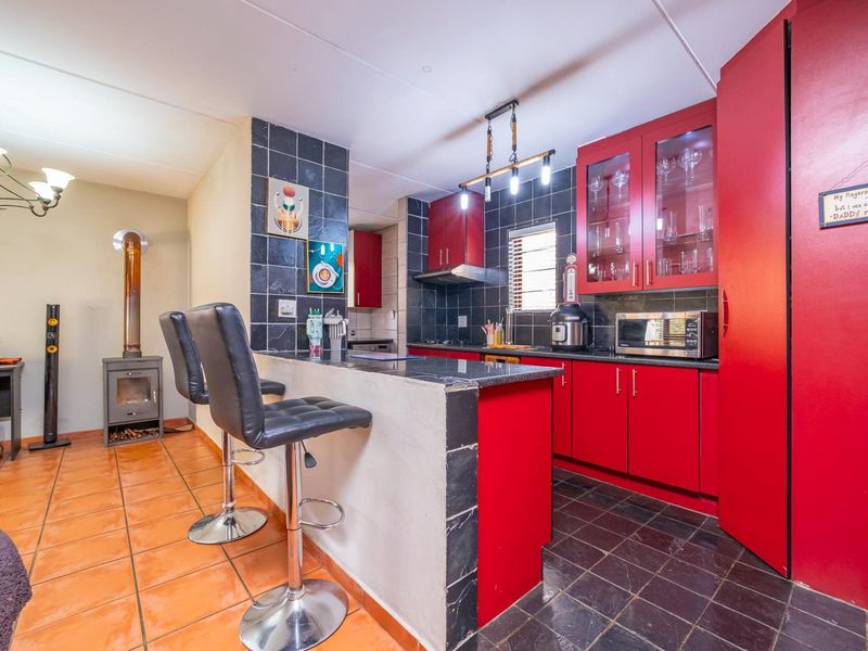 Open-plan kitchen featuring vibrant red cabinetry, granite countertops, and a breakfast bar, seamlessly connected to a living area with a wood-burning fireplace.