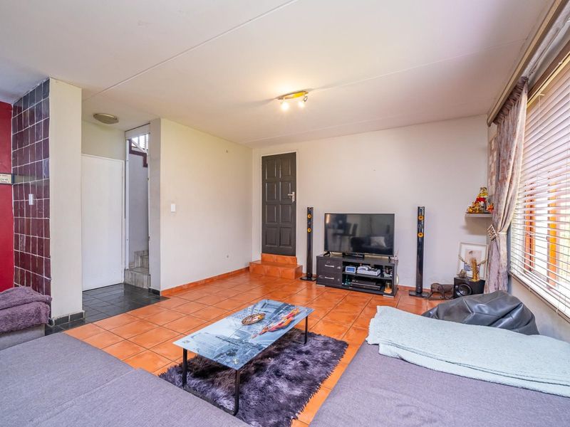 A living room featuring tiled flooring, venetian blinds, and access to an internal staircase, offering a functional space with potential for cosmetic updates.
