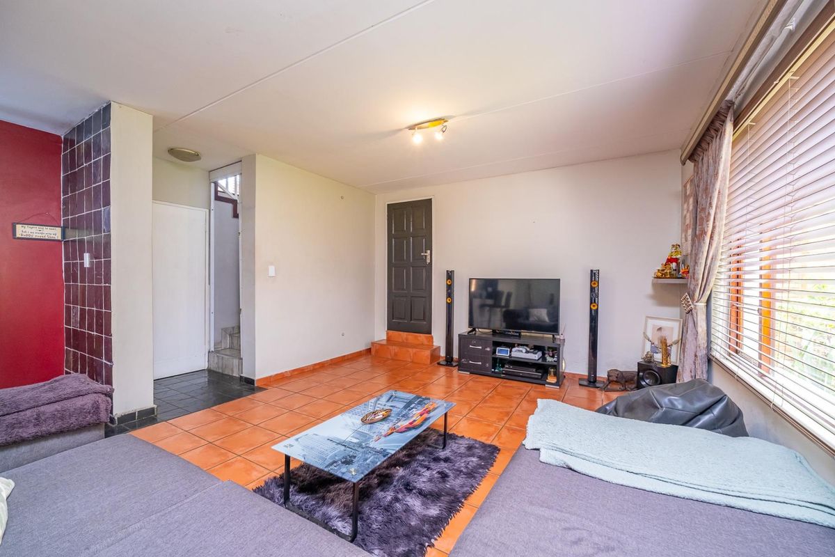A living room featuring tiled flooring, venetian blinds, and access to an internal staircase, offering a functional space with potential for cosmetic updates.