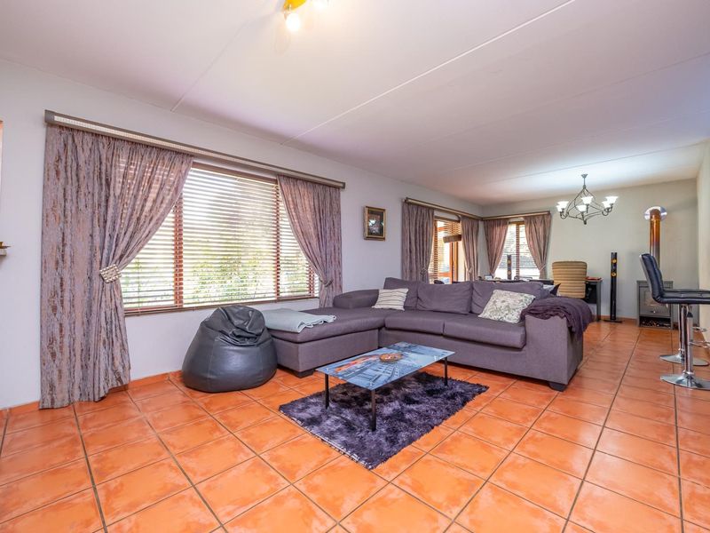 Spacious open-plan living area featuring terracotta floor tiles, a wood-burning fireplace, and large windows with venetian blinds.