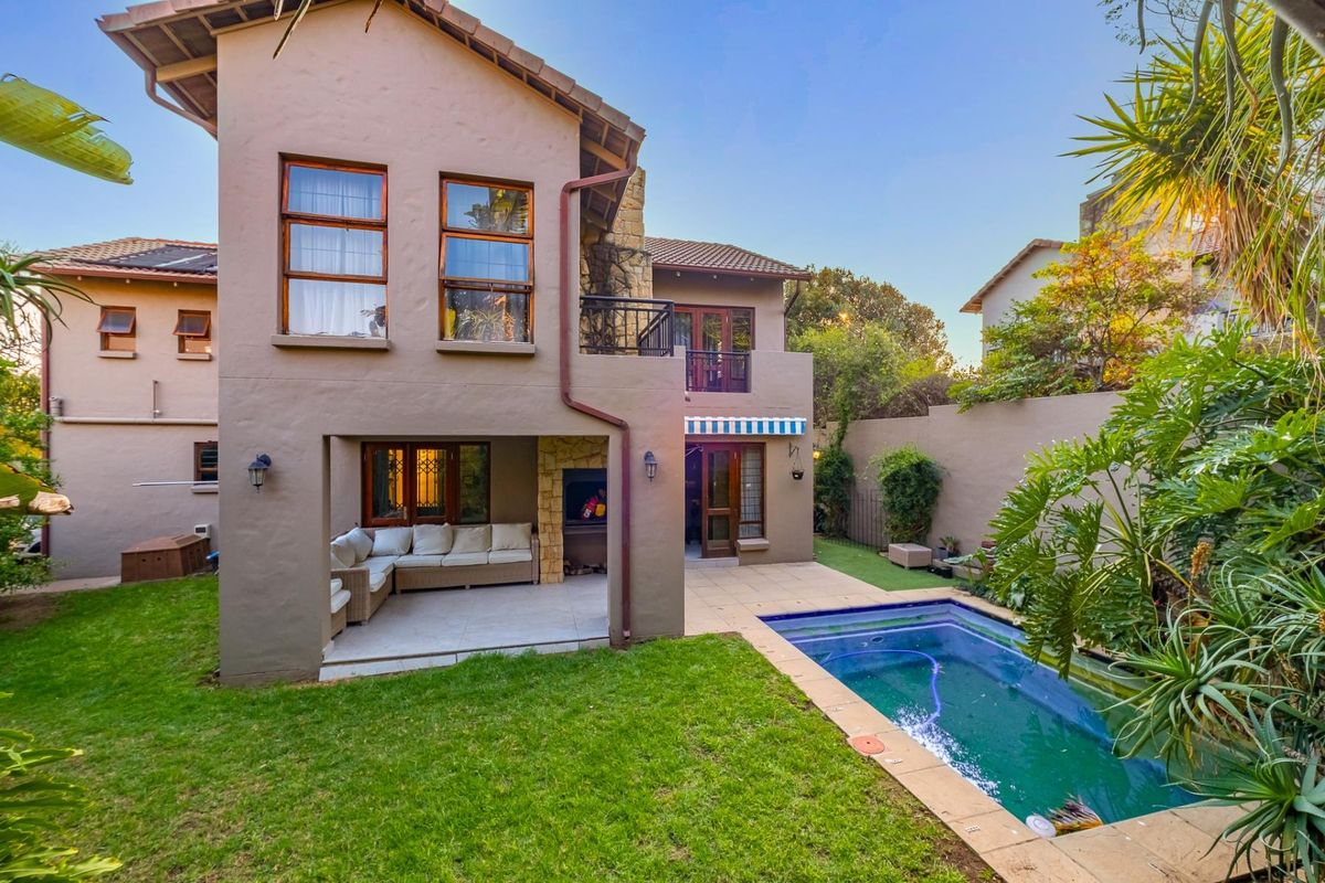 Rear view of a double-story house featuring a covered patio with built-in braai, a swimming pool, and a well-maintained garden.