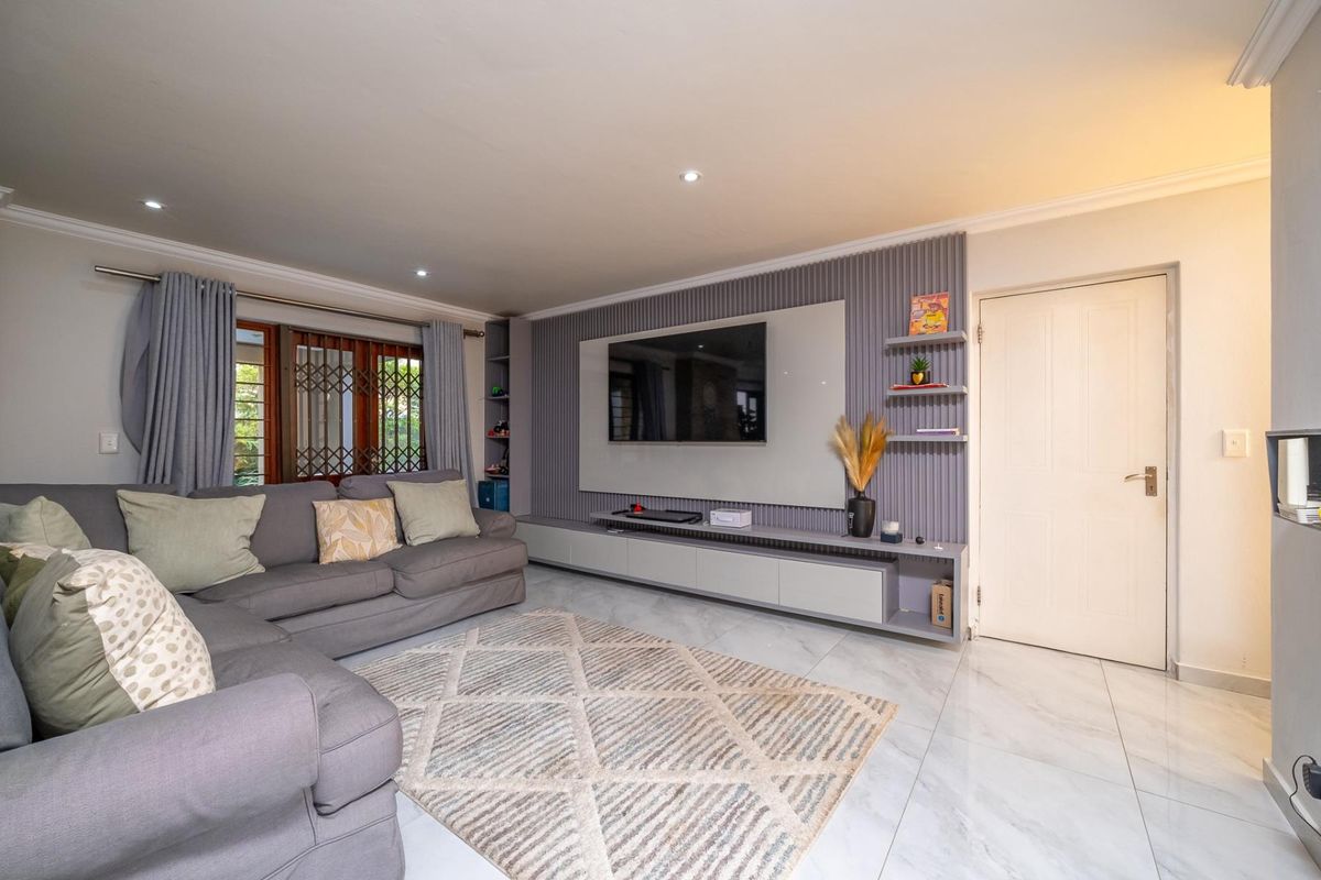 A modern living room featuring a sleek built-in media wall, recessed downlighting, and polished tiled flooring.