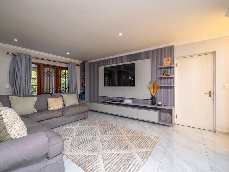 A modern living room featuring a sleek built-in media wall, recessed downlighting, and polished tiled flooring.