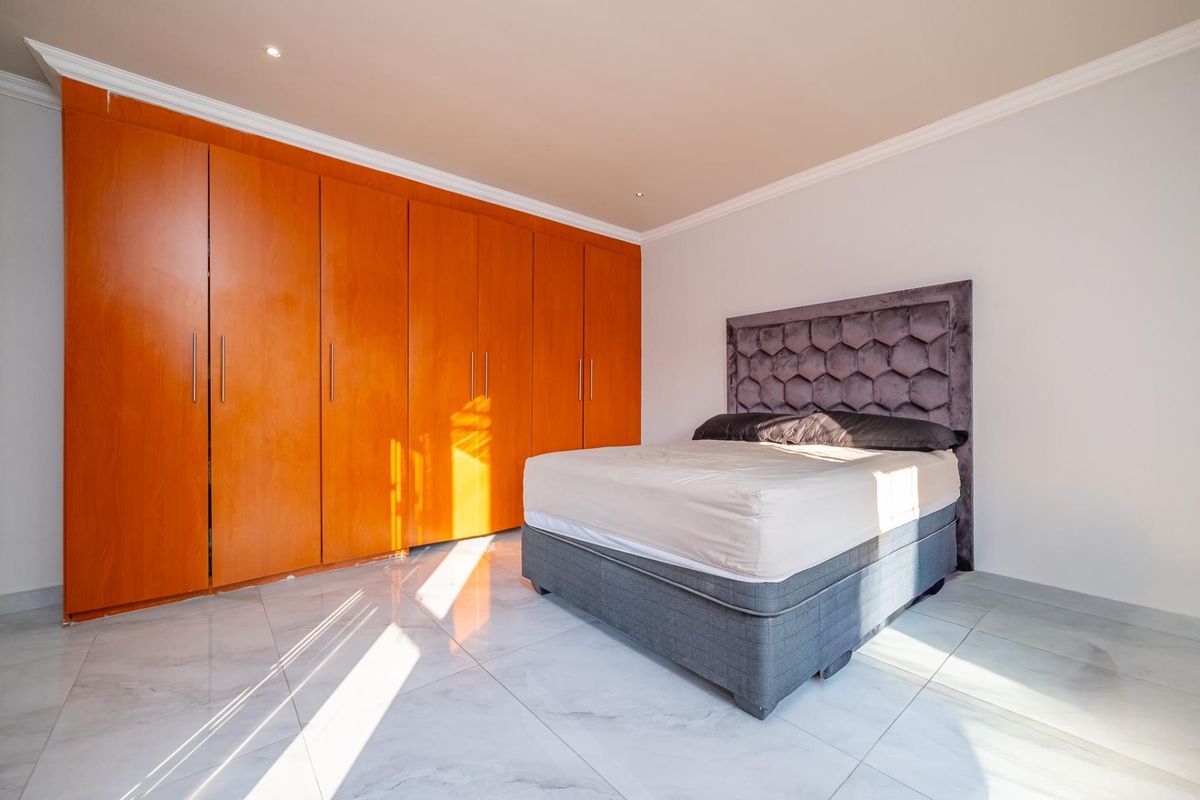 A well-maintained bedroom featuring large built-in wooden cupboards, polished tiled flooring, and recessed ceiling lighting.