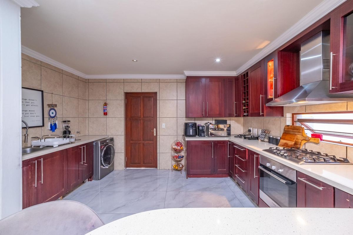 A functional kitchen featuring dark wood cabinetry, stone countertops, a gas hob, built-in oven, and tiled finishes throughout.