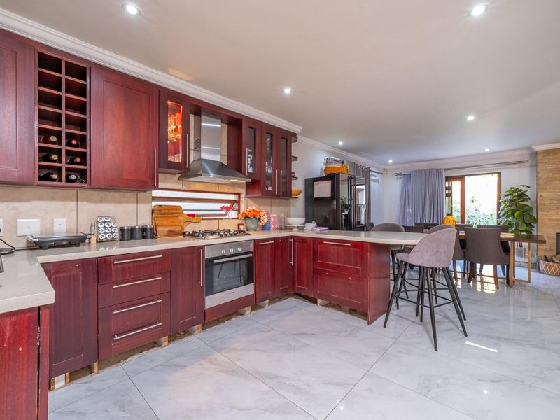 Spacious open-plan kitchen and dining area featuring dark wood cabinetry, stone countertops, modern tiled flooring, and a stone feature wall with a fireplace.