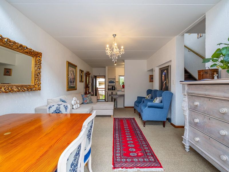 Open-plan living and dining area featuring a central chandelier, carpeted flooring, and a view through to the kitchen and rear access.