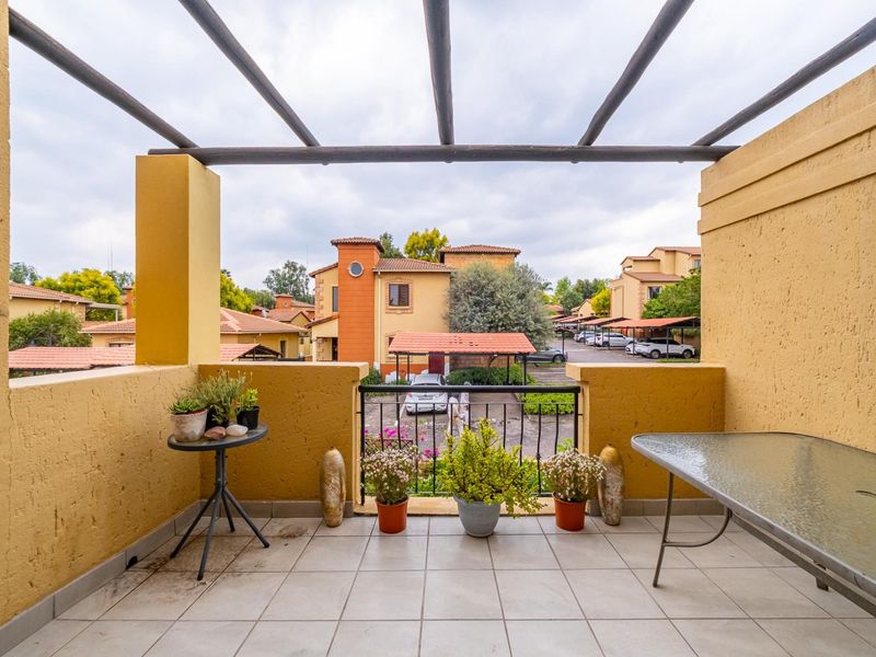 Covered balcony featuring a pergola structure, tiled flooring, and metal railings, offering views over the complex grounds.