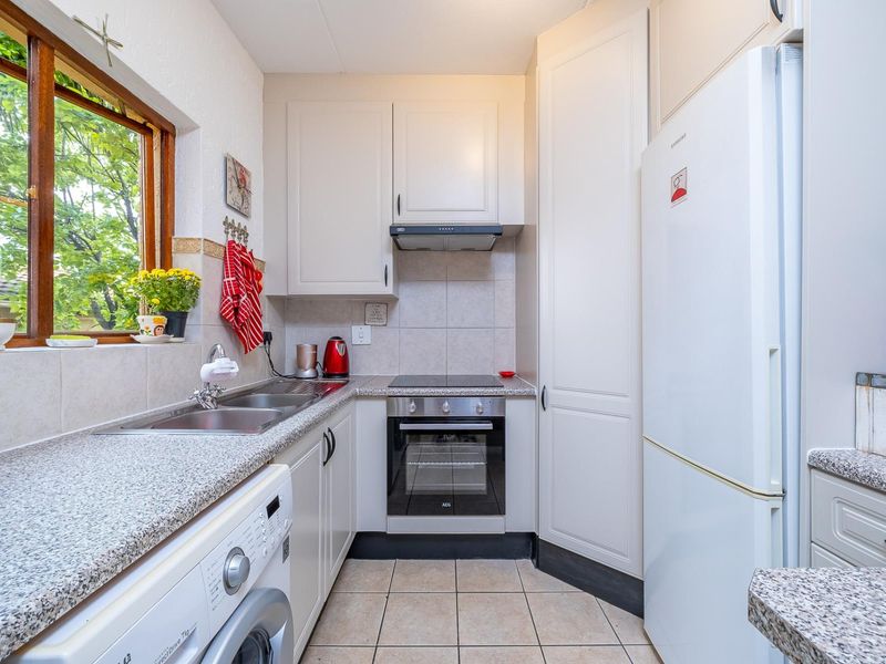 Compact kitchen featuring built-in cabinetry, granite countertops, integrated oven and hob, and tiled flooring with a window overlooking the garden.
