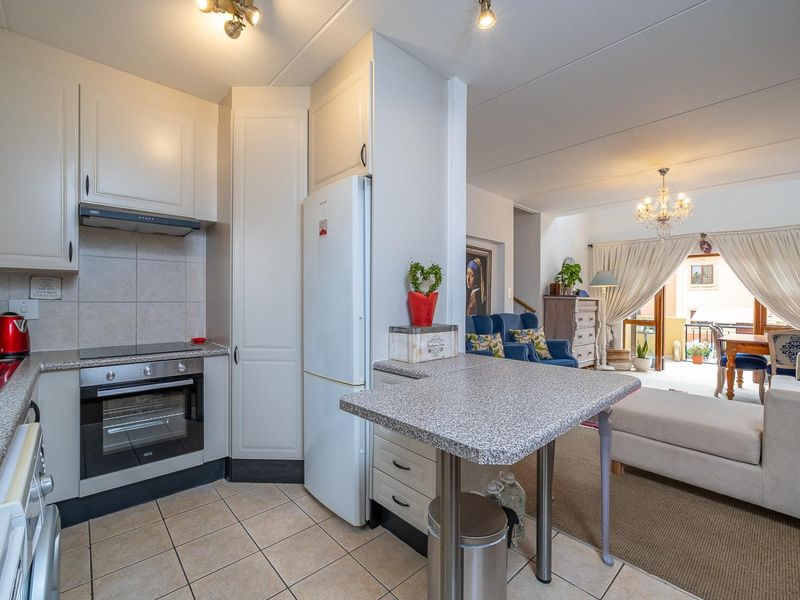 Open-plan kitchen featuring neutral cabinetry, laminate countertops, and integrated appliances, flowing seamlessly into the adjacent living and dining area with balcony access.