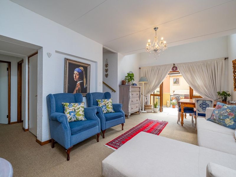 Spacious open-plan living and dining area featuring a chandelier, neutral carpeting, and direct access to an outdoor balcony through sliding glass doors.