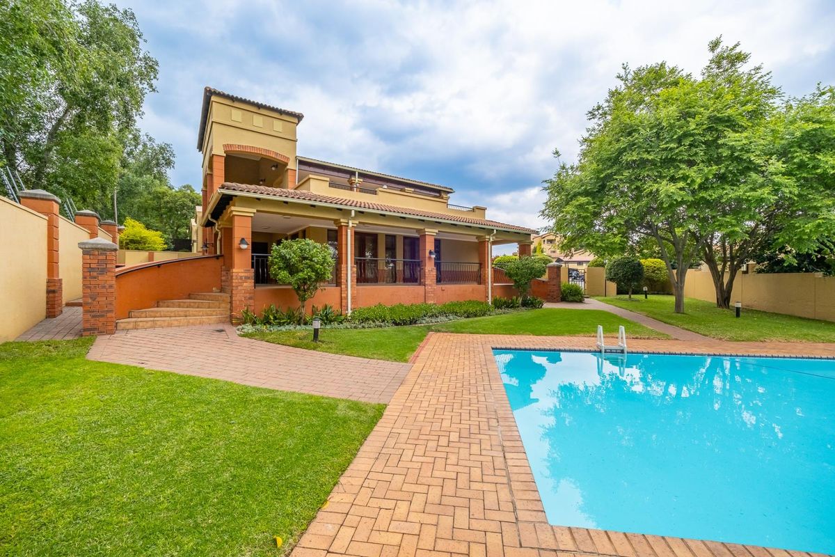 A well-maintained rear exterior view featuring a swimming pool, brick-paved patio, covered veranda, and landscaped garden area.