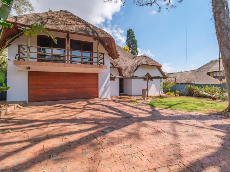 Front exterior view of a house featuring a distinctive thatched roof, brick paved driveway, integrated garage, and an upper-level balcony with wooden balustrade.