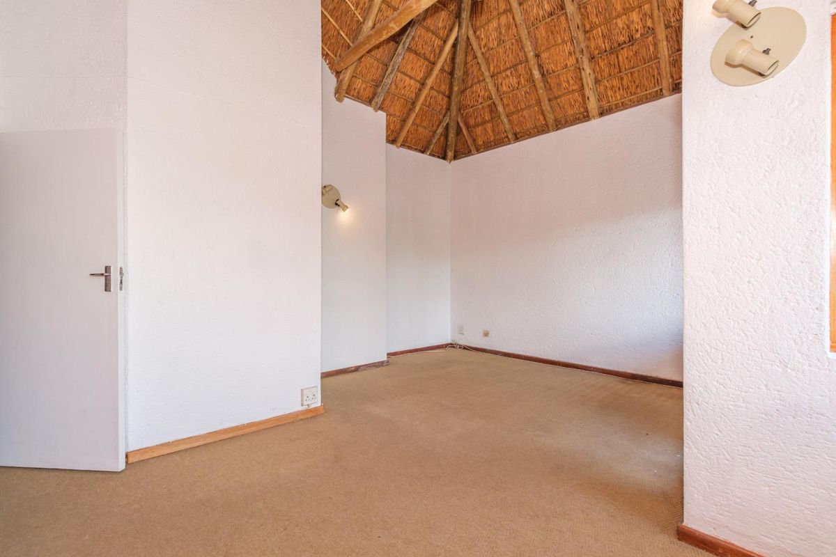 An empty bedroom featuring a high thatched ceiling with exposed timber rafters, neutral walls, and carpeted flooring.