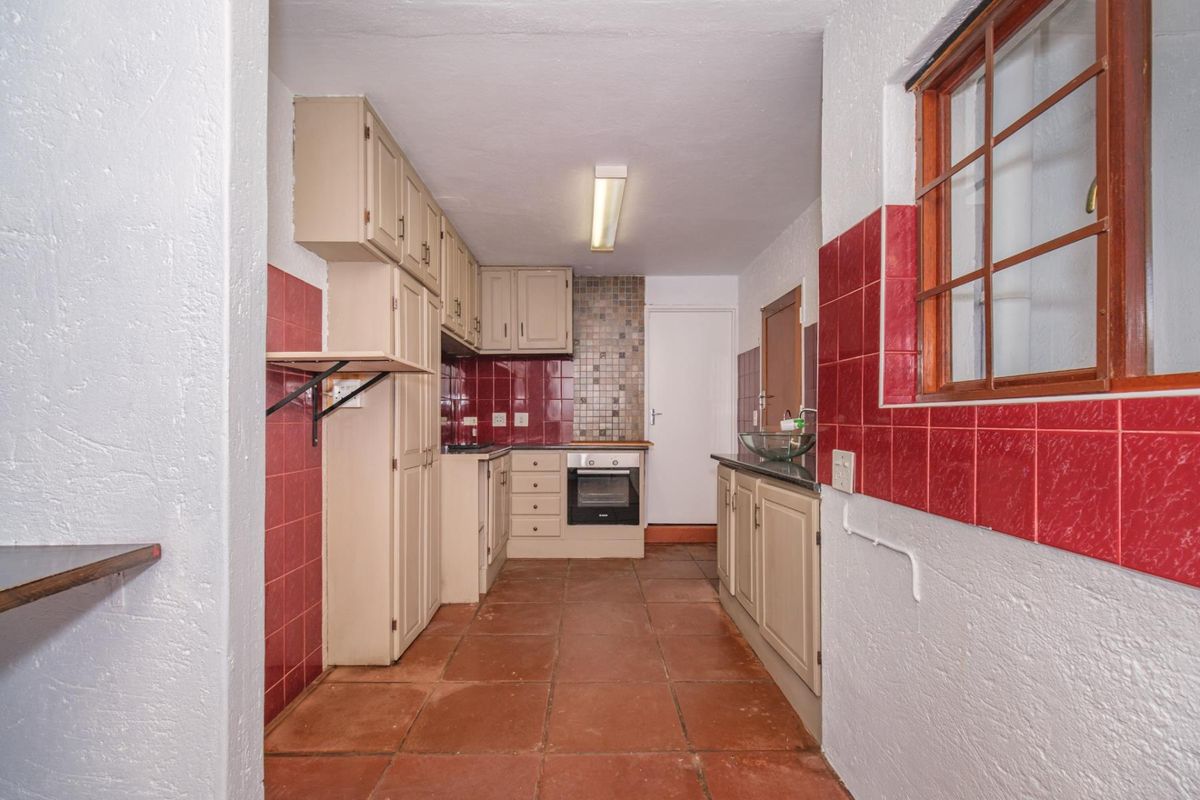 A functional kitchen featuring built-in cabinetry, a built-in oven, hob, and terracotta floor tiles, offering a blank canvas for modern renovation.