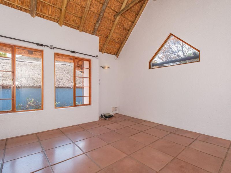 Spacious living area featuring a high vaulted thatched ceiling with exposed rafters, tiled flooring, and unique timber-framed windows providing natural light.