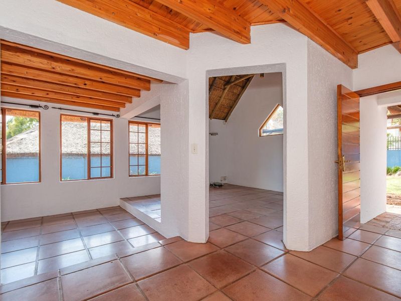 An open-plan living area featuring exposed timber ceiling beams, terracotta floor tiles, and natural light through multiple timber-framed windows.