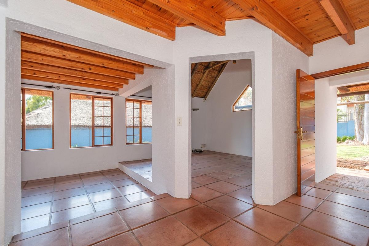 An open-plan living area featuring exposed timber ceiling beams, terracotta floor tiles, and natural light through multiple timber-framed windows.
