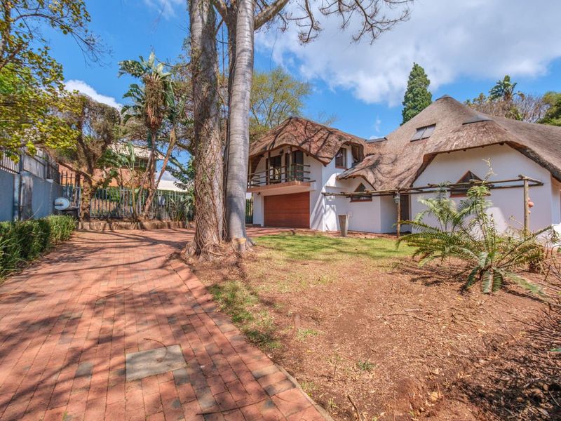 Front view of a unique thatched-roof house featuring a brick-paved driveway, integrated garage, and an upper-level balcony.