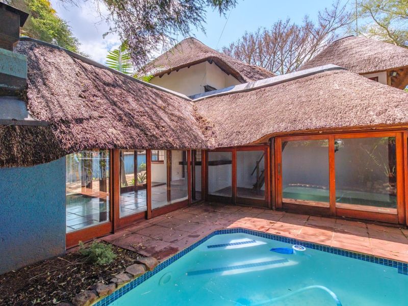 Outdoor pool area featuring a swimming pool, tiled patio, and extensive sliding glass doors under a traditional thatched roof structure.