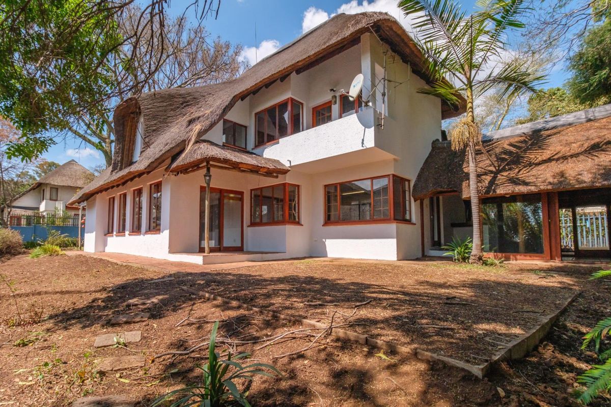Rear view of a two-story house featuring a traditional thatched roof, timber-framed windows, and a balcony overlooking the garden area.