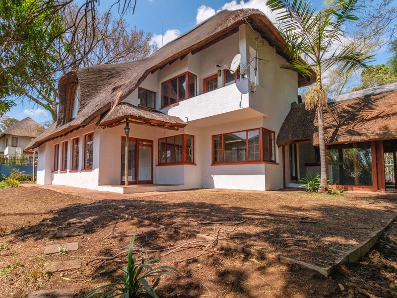 Rear view of a two-story house featuring a traditional thatched roof, timber-framed windows, and a balcony overlooking the garden area.