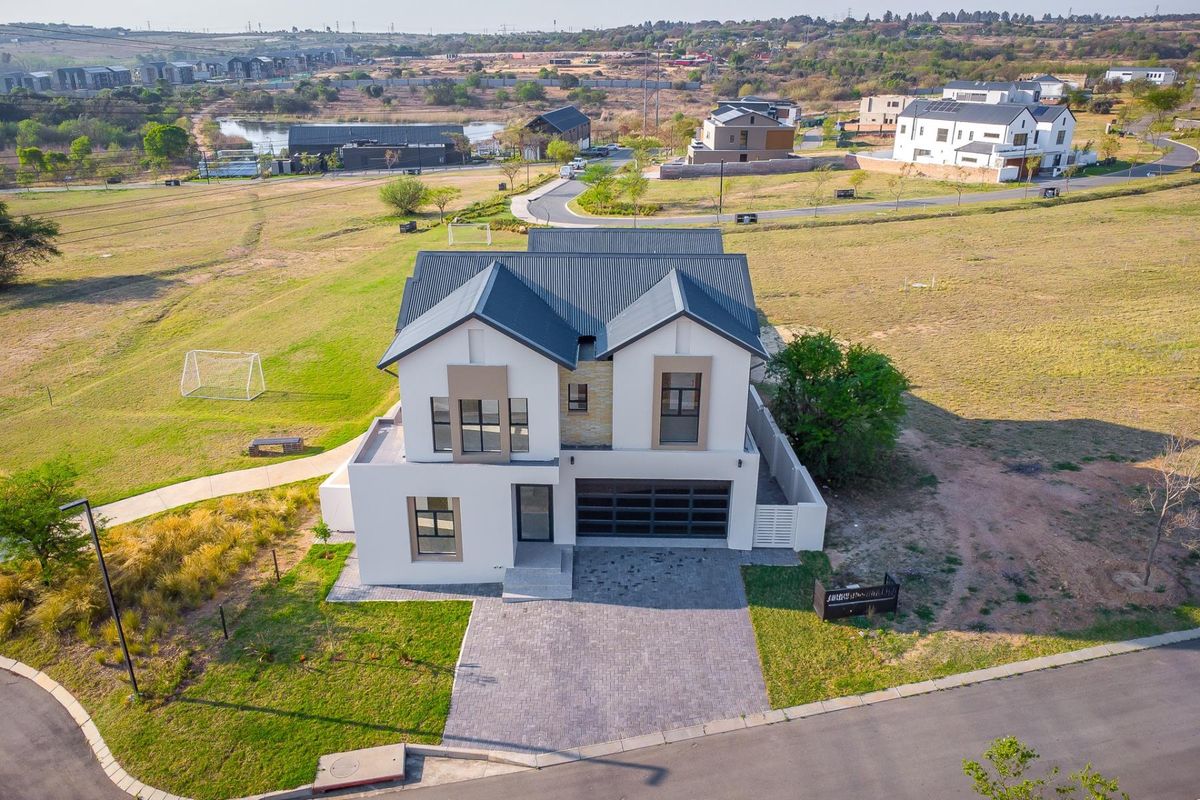 Aerial view of a modern two-story residential house featuring a metal roof, stone accents, and a paved driveway in a suburban estate setting.