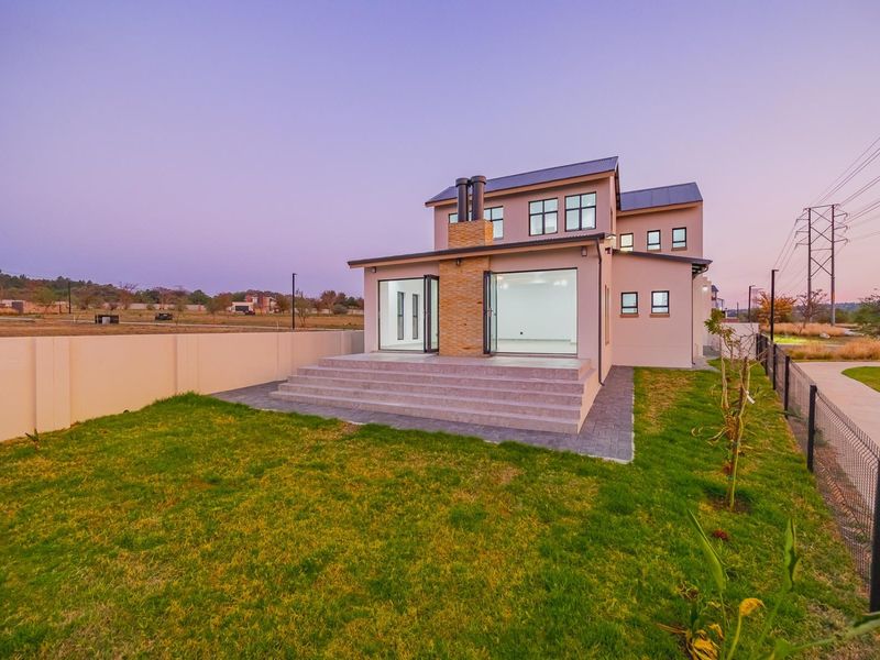 Rear view of a modern two-story house featuring a stone-clad chimney, concrete patio steps, and large bi-fold glass doors opening to a landscaped garden.