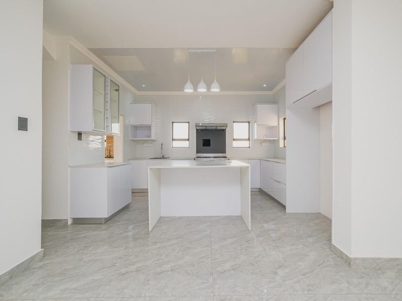 A modern, bright kitchen featuring white cabinetry, a central island, stone countertops, and high-quality tiled flooring in a clean, minimalist design.