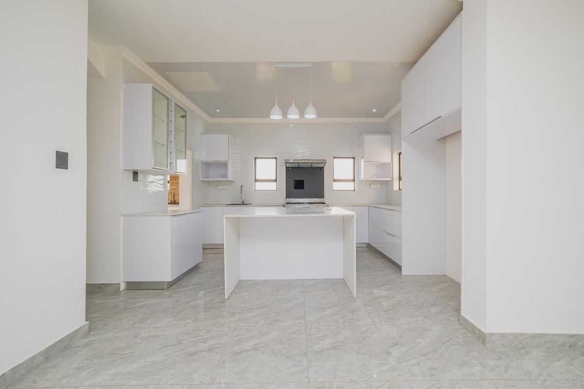 A modern, bright kitchen featuring white cabinetry, a central island, stone countertops, and high-quality tiled flooring in a clean, minimalist design.