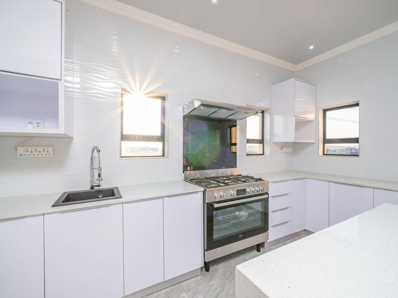 Modern kitchen featuring white cabinetry, stone countertops, a gas stove with extractor fan, and high-quality finishes throughout.