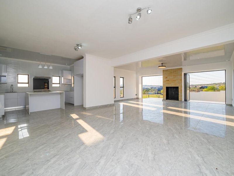 Spacious open-plan living area featuring a modern kitchen with island, stone fireplace, and large sliding doors leading to an outdoor space.