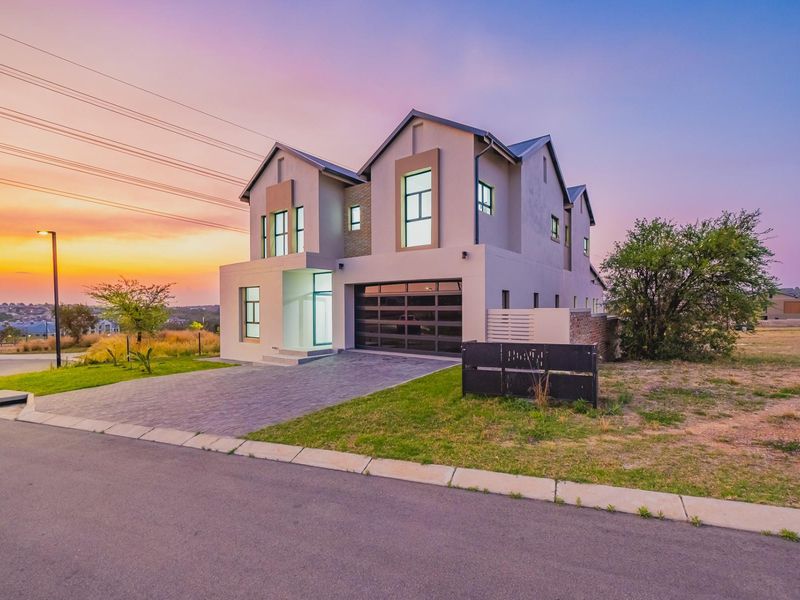 Modern double-story residential home featuring a paved driveway, double garage, and contemporary architectural design set against a sunset backdrop.
